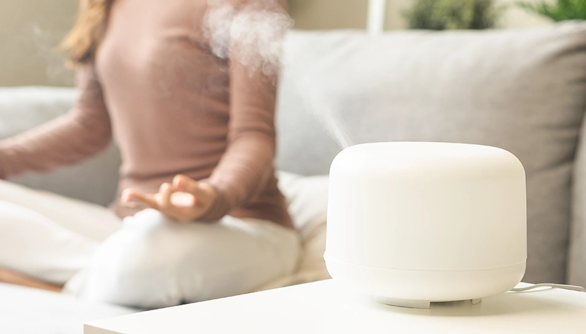 Mujer haciendo yoga en su casa con un humidificador puesto en su salón. con aposán, humedad controlada